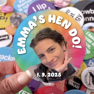 May include: A circular pin-back button featuring a rainbow-colored radial background. The text "EMMA'S HEN DO!" is printed in white along the top curve, and the date "1.9.2025" is printed in white at the bottom. A photograph of a person is centered.