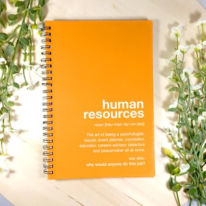 Puede incluir: Cuaderno naranja con encuadernación en espiral. La portada tiene el texto "human resources" con una definición y la pregunta "why would anyone do this job?"