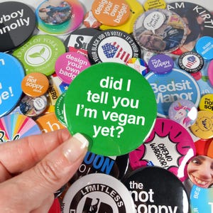 May include: A collection of colourful button badges with various designs and messages. One badge is green and reads "did I tell you I'm vegan yet?"