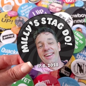 May include: A circular pinback button featuring a photograph of a smiling person. The background has a black and gray spiral pattern. The text "MILLY'S STAG DO!" is printed in white at the top, and the date "17. 5. 2025" is printed in white at the bottom.