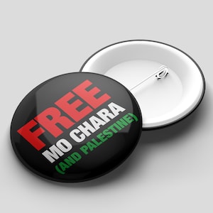 Może przedstawiać: Dwie okrągłe czarne przypinki z białymi obwódkami. Jedna przypinka wyświetla słowa "FREE MO CHARA (AND PALESTINE)" w kolorze czerwonym, białym i zielonym. Druga przypinka jest biała z metalową szpilką.