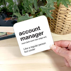 Könnte beinhalten: Weißer Untersetzer mit schwarzem Text, der "account manager" lautet und eine Definition des Wortes. Die Definition lautet "Substantiv [ack-ount man-adge-err] Wie eine normale Person, aber cooler."