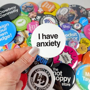 Puede incluir: Una colección de botones coloridos con varios diseños y mensajes, que incluyen "Tengo ansiedad", "no soy sensiblero", "guerrero de quimioterapia" y "diseña tu propia insignia".