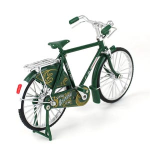 May include: A miniature green vintage bicycle with silver handlebars and wheels. The bicycle has a luggage rack and a seat. The words "Vintage Shanghai" are printed on the side of the bicycle.