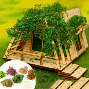 May include: A miniature wooden cabin with a green ivy roof and a wooden deck. The cabin has a window and a door. The deck has a railing and steps. There are several small bunches of green, brown, and pink moss on the ground in front of the cabin.