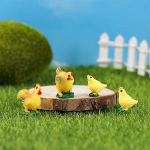 May include: Four miniature yellow ceramic chickens, two standing upright and two in a sitting position, on a brown wooden surface. The chickens have red beaks and black eyes.