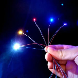 May include: Five strands of thin, colorful wire with small LED lights at the end. The lights are red, blue, yellow, and white.