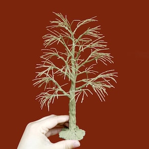 May include: A small tree sculpture with a textured, pale green trunk and branches. The branches are slender and spread outwards, giving a delicate, natural look. The tree is set against a reddish-brown background.