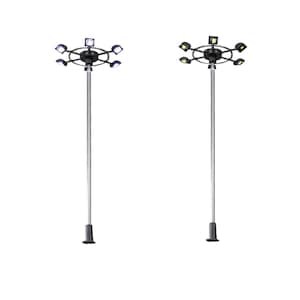May include: Two tall, silver light poles with black fixtures. Each pole has a circular array of lights at the top. The lights are white and bright, suitable for outdoor illumination. The poles stand against a white background.