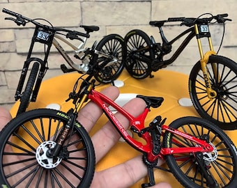 May include: Miniature mountain bikes in red, black, and silver with black tires and gold suspension forks. Each bike has the number 33 on the handlebars. The bikes are displayed on a yellow surface.