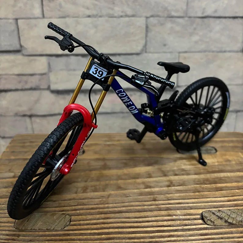 May include: Miniature mountain bike with a blue frame, gold suspension, and red fork. The bike has black tires and handlebars, with the number 39 on the front. The words "COME ON" are printed on the frame.
