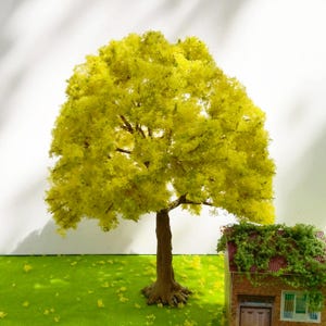 Peut inclure: Une maquette miniature d'un arbre avec un feuillage jaune-vert et un tronc brun. L'arbre se trouve à côté d'une petite maison en briques avec un toit rouge recouvert de vignes vertes. La scène est posée sur une surface verte.