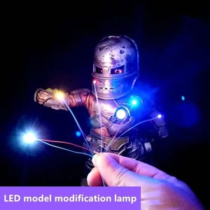 Op de afbeelding: Een metalen Iron Man actiefiguur met LED-verlichting. De figuur heeft een verweerde uitstraling en wordt verlicht met blauwe en witte lichten. De tekst "LED model modification lamp" is zichtbaar onderaan de afbeelding.