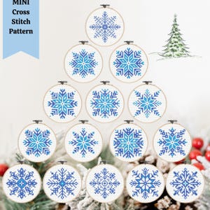 May include: Twelve blue and white snowflake cross stitch patterns in round embroidery hoops.  The hoops are arranged in a Christmas tree shape.  "MINI Cross Stitch Pattern" is written at the top of the image.