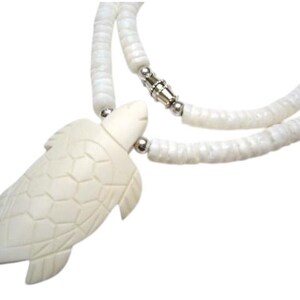 May include: Cream-colored turtle pendant necklace. The pendant is carved with detailed shell patterns and is strung on a double strand of white, disc-shaped beads. The necklace has a silver-tone clasp.
