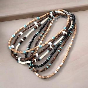 May include: A multi-strand necklace made of brown, black, and white wooden beads with turquoise accents. The necklace is layered and has a casual, bohemian style.