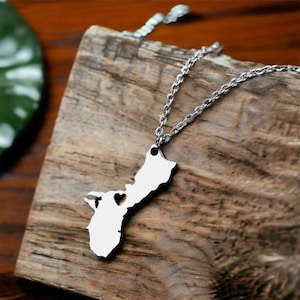 May include: A silver necklace with a pendant shaped like the island of Guam. The pendant has a small heart cut out of it.