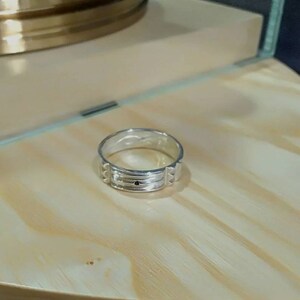Pu&ograve; includere: Un anello a fascia d'argento con un design testurizzato e una piccola pietra nera al centro.