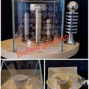 Pu&ograve; includere: Un generatore di biocampo dorato in un cubo di vetro su una base di legno. Il generatore ha un design a spirale ed &egrave; circondato da spirali pi&ugrave; piccole. La base ha le parole "Biofield Generator" scritte su di essa.