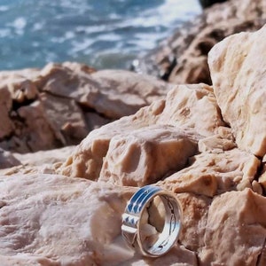 Pu&ograve; includere: Un anello d'argento con un designo testurizzato, appoggiato su una superficie rocciosa. L'anello &egrave; fatto di metallo e ha un motivo unico e intricato.