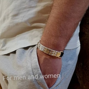 Könnte beinhalten: Ein silbernes Armband mit einem schwarzen Lederband. Das Armband hat ein geometrisches Design und wird am Handgelenk getragen.