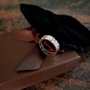 Pu&ograve; includere: Un anello d'argento con un designo testurizzato e una piccola pietra trasparente incastonata al centro. L'anello &egrave; esposto in una scatola marrone con un sacchetto di velluto nero.