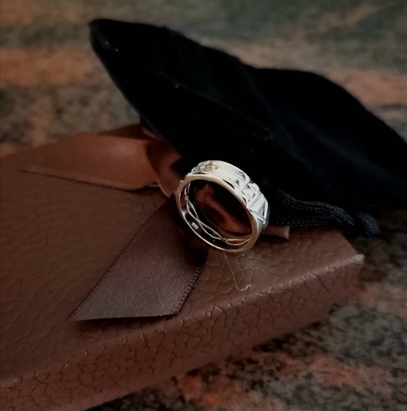 Pu&ograve; includere: Un anello d'argento con un designo testurizzato e una piccola pietra trasparente incastonata al centro. L'anello &egrave; esposto in una scatola marrone con un sacchetto di velluto nero.