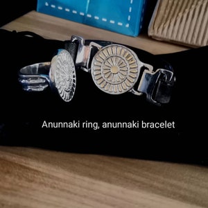 Op de afbeelding: Een zilveren ring en armband met een gouden zonontwerp. De tekst "Anunnaki ring, anunnaki bracelet" is zichtbaar onder de sieraden.