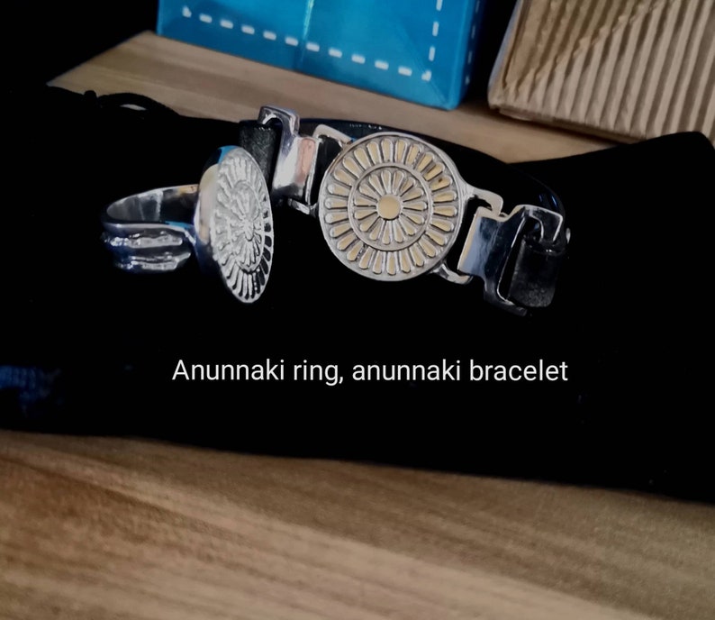 Op de afbeelding: Een zilveren ring en armband met een gouden zonontwerp. De tekst "Anunnaki ring, anunnaki bracelet" is zichtbaar onder de sieraden.