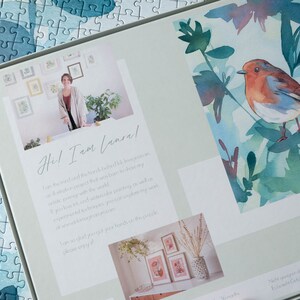 May include: A white box with a watercolor painting of a robin on a branch with green leaves. The box also features a photo of the artist and text that reads "Hel I am (ansal" and "I am so glad you got your arches pack, please enjoy!"
