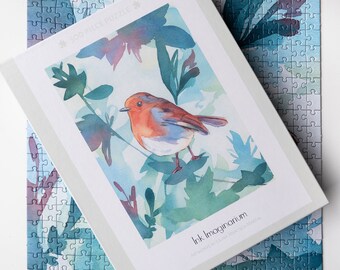 May include: A 50-piece jigsaw puzzle featuring a watercolor painting of a robin perched on a branch with green leaves. The puzzle box has the title "Ink Imaginarium" and the artist's name "Laura Jane McLaughlin".