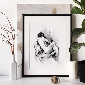 May include: Black and white ink drawing of two figures in a romantic embrace, framed in a black frame and displayed on a white wall with a plant and a vase.