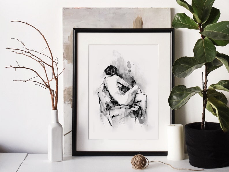 May include: Black and white ink drawing of two figures in a romantic embrace, framed in a black frame and displayed on a white wall with a plant and a vase.