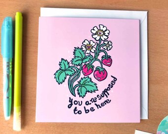 May include: Pink greeting card featuring a cartoon illustration of a strawberry plant with flowers and strawberries. The text on the card reads "You are supposed to be here."