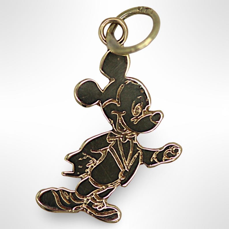 Puede incluir: Un dije de Mickey Mouse de tono dorado. El dije presenta una silueta detallada de Mickey Mouse con un esmoquin, caminando con el brazo derecho extendido.