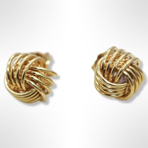 May include: A pair of gold knot-shaped earrings. The earrings are made of a woven design and have a shiny finish.