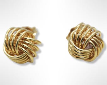 May include: A pair of gold knot-shaped earrings. The earrings are made of a woven design and have a shiny finish.