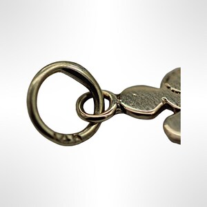 Puede incluir: Encanto de plata con un bucle redondo y una figura estilizada de una persona. El encanto est&aacute; hecho de plata y tiene un acabado brillante.