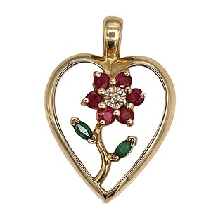 May include: A gold pendant in the shape of a heart, featuring a flower design. The flower has red ruby petals and a diamond center. The stem and leaves are gold with green emerald accents.