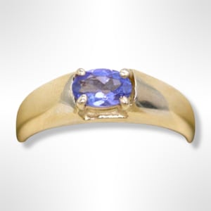 Puede incluir: Un anillo de banda de oro con una piedra preciosa ovalada de color azul claro.