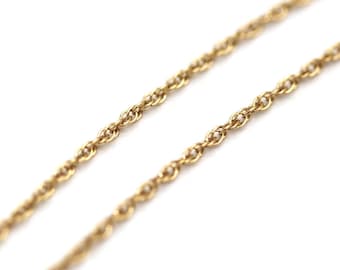 May include: Close-up of a gold-colored rope chain necklace. The chain is made of small, interconnected links, creating a textured surface. The necklace is set against a white background, highlighting its color and design.