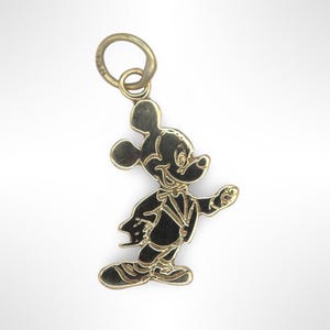 Puede incluir: Un dije de Mickey Mouse de tono dorado. El dije presenta una silueta detallada de Mickey Mouse con un esmoquin, caminando con el brazo derecho extendido.