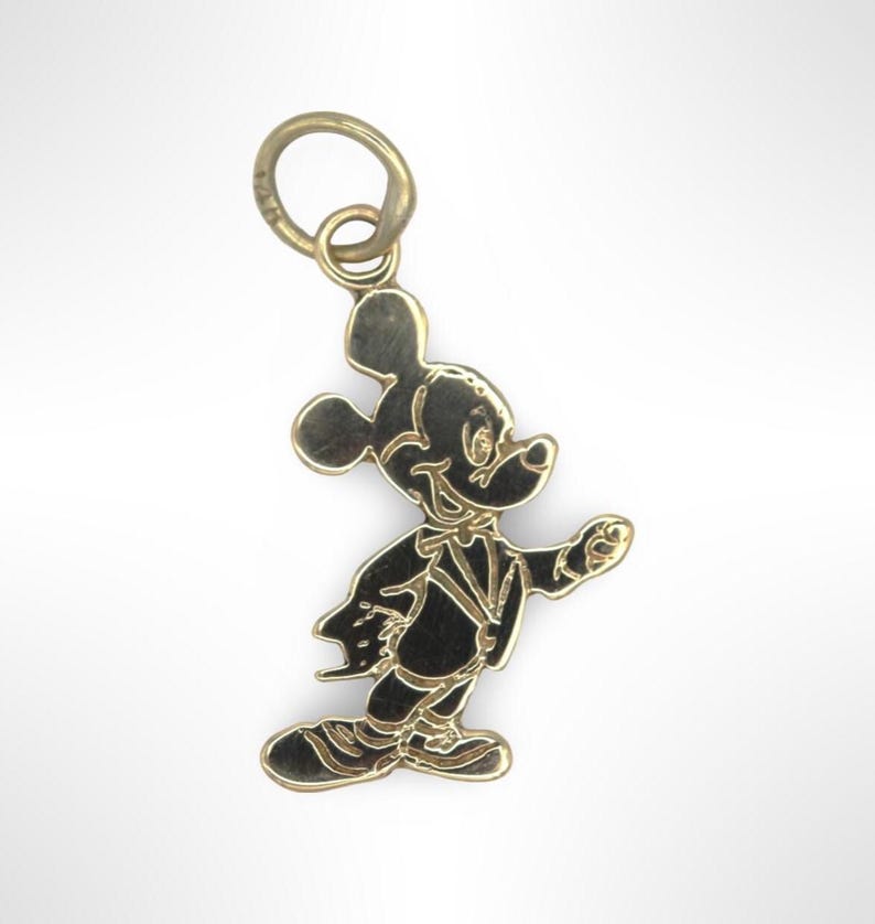 Puede incluir: Un dije de Mickey Mouse de tono dorado. El dije presenta una silueta detallada de Mickey Mouse con un esmoquin, caminando con el brazo derecho extendido.