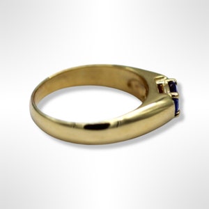 Puede incluir: Un anillo de banda de oro con una sola piedra preciosa azul oscuro de forma cuadrada engastada en el centro.