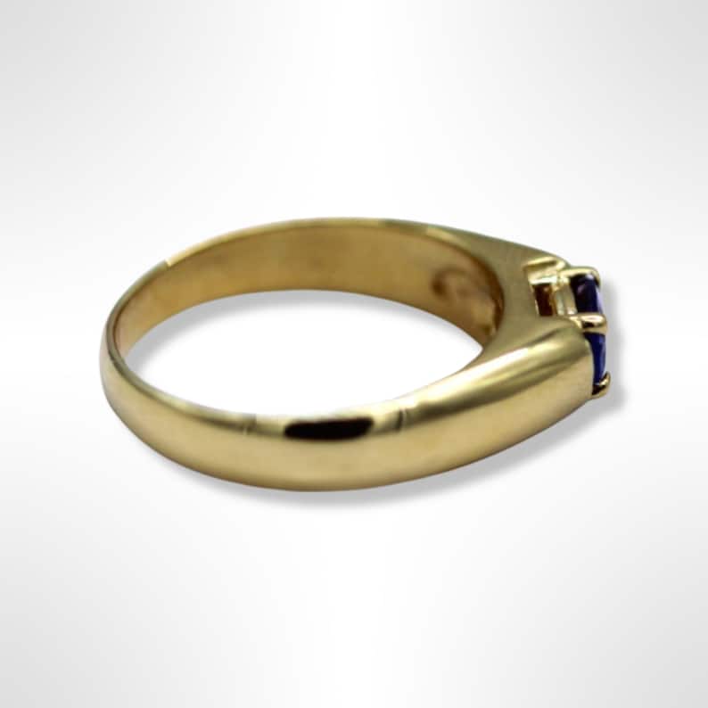 Puede incluir: Un anillo de banda de oro con una sola piedra preciosa azul oscuro de forma cuadrada engastada en el centro.