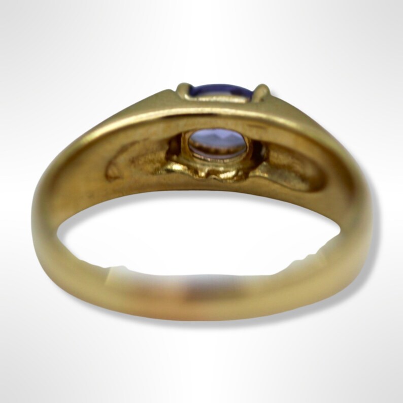 Puede incluir: Un anillo de oro con una piedra preciosa p&uacute;rpura engastada en el centro. El anillo se ve desde abajo, mostrando la parte inferior de la banda.