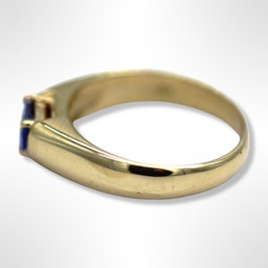 Puede incluir: Un anillo de oro con una piedra preciosa azul engastada en el centro. El anillo tiene un dise&ntilde;o simple y cl&aacute;sico.