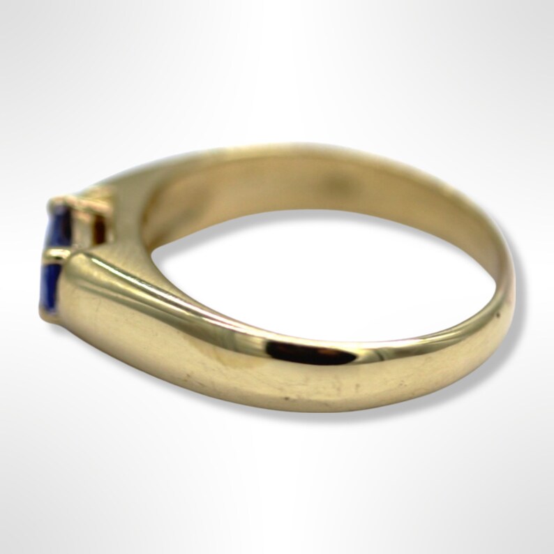 Puede incluir: Un anillo de oro con una piedra preciosa azul engastada en el centro. El anillo tiene un dise&ntilde;o simple y cl&aacute;sico.