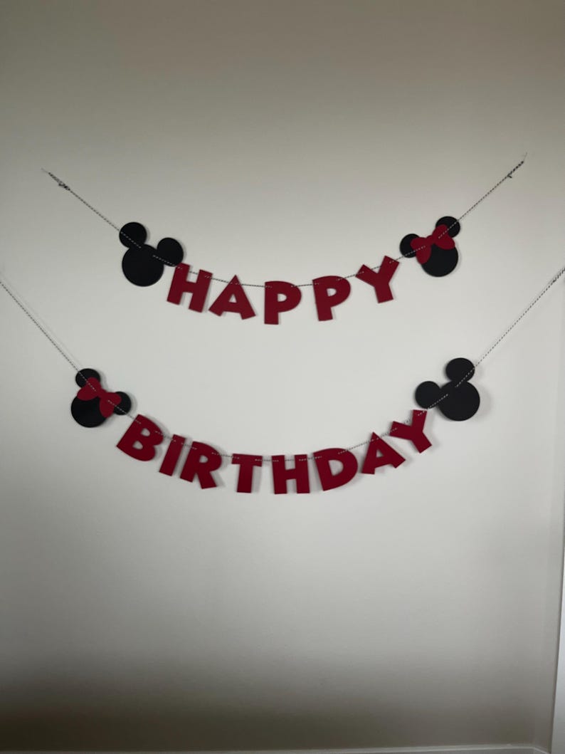 Puede incluir: Bandera de fieltro rojo con las palabras "Happy Birthday" y siluetas negras de Mickey Mouse y Minnie Mouse.