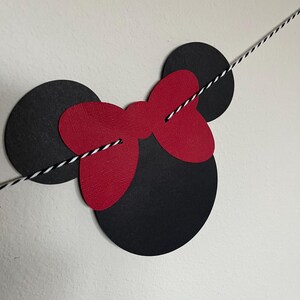 Puede incluir: Recortes de papel negro y rojo de orejas de Mickey Mouse y un lazo, ensartados con un cordel blanco y negro.